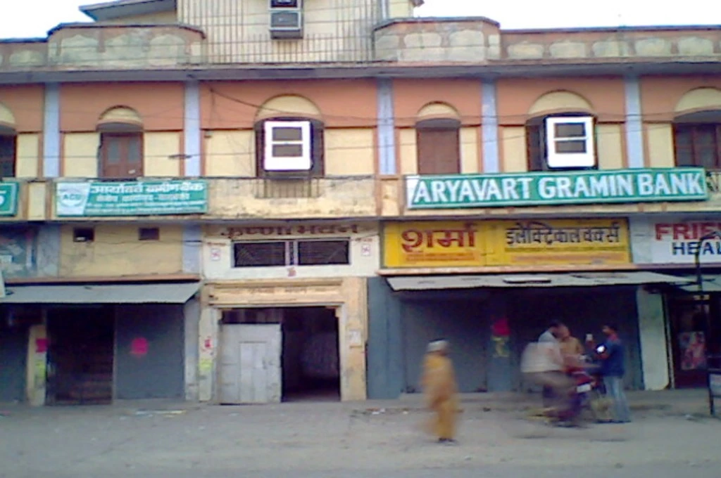 The image shows a building with a few shops. Above one of the shops, there is a sign that reads 'Aryavart Gramin Bank'.