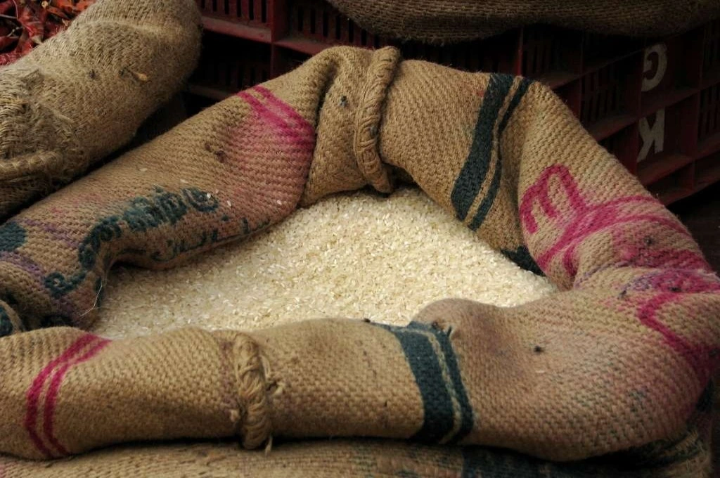The image is a close-up of a burlap sack filled with grains of rice._Ration