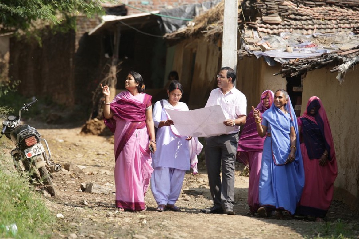 One man holding a chart and a few village women talking to him