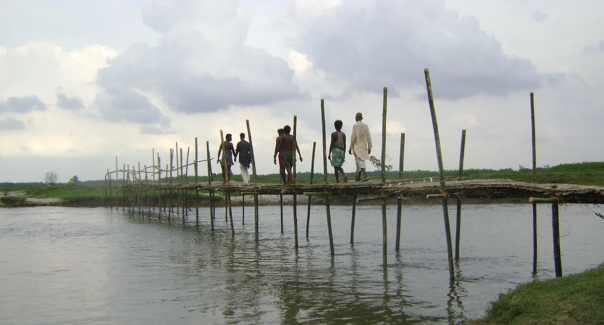A few men walking on a thin bridge built in the middle of the lake