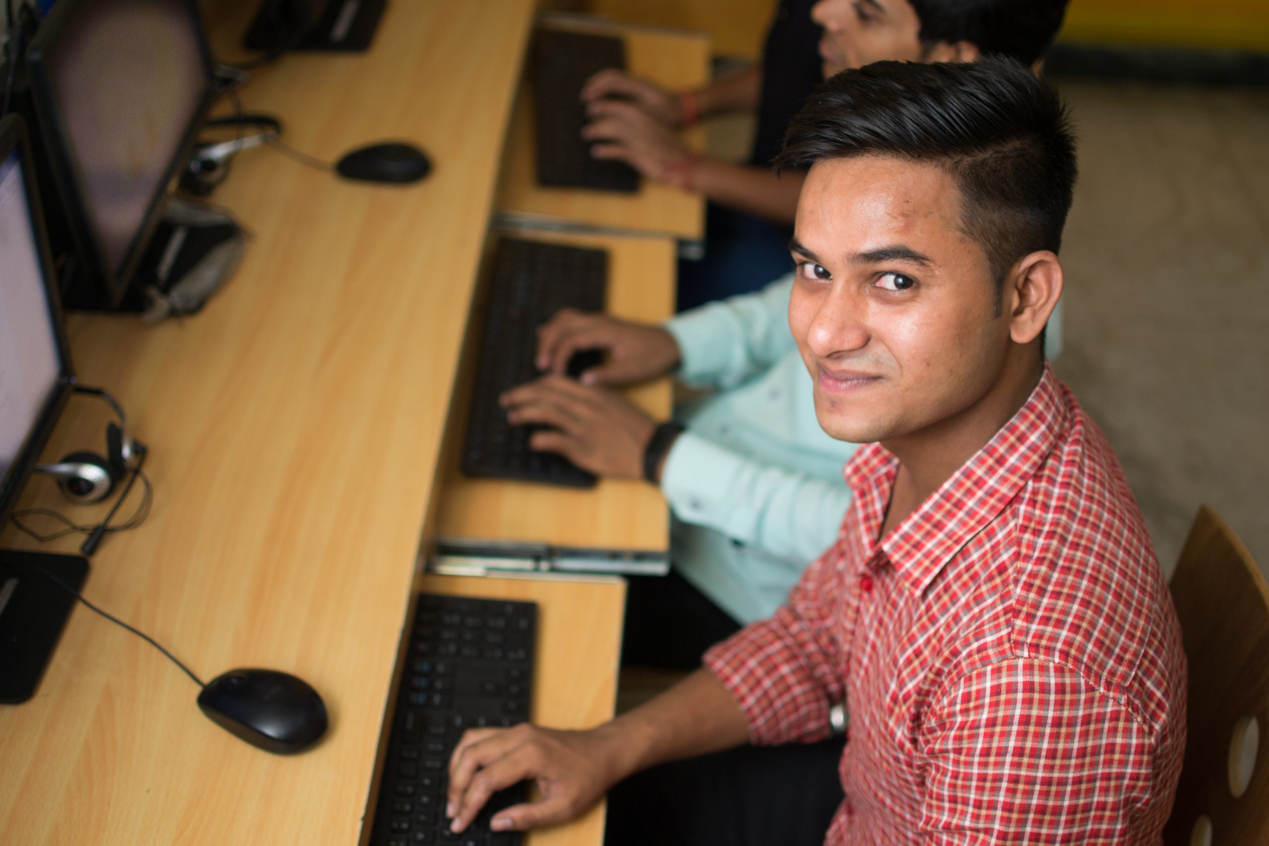 Young boy in checked shirt, sitting at computer, looks up into the camera. Employability training should focus on skilling the youth