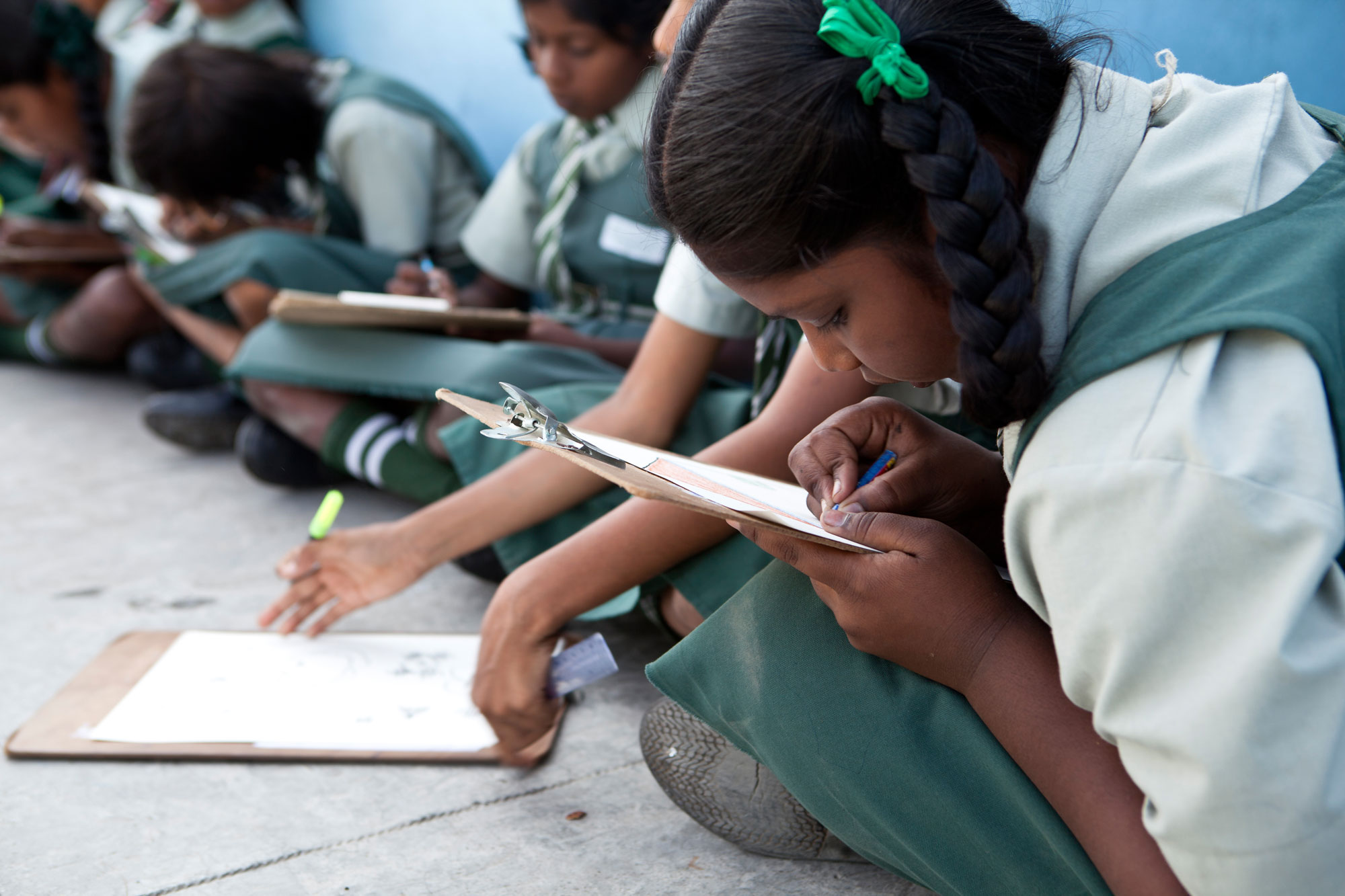 A girl writing on a paper placed on a board, sitting in a row with other girls engaged in writing. Empowering adolescent women: A data-backed guide to successful methods