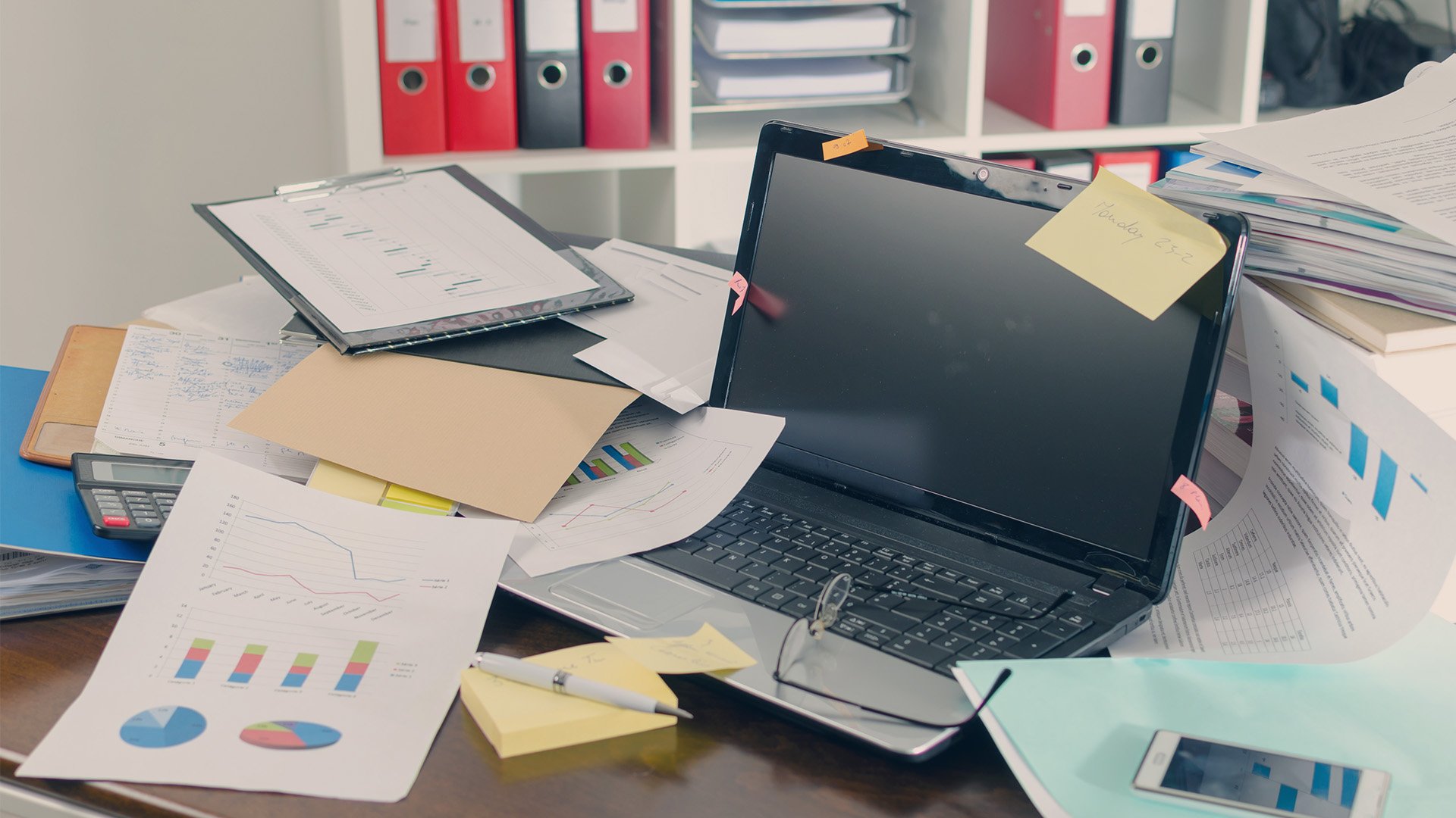 A cluttered work desk with laptops and sheets of data