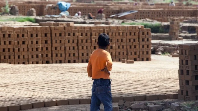 image of child standing and looking at a stack of bricks-child labour