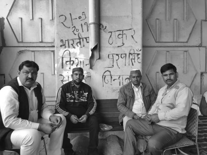 Four people looking into the camera with slogans written on the walls behind them-farmers protest