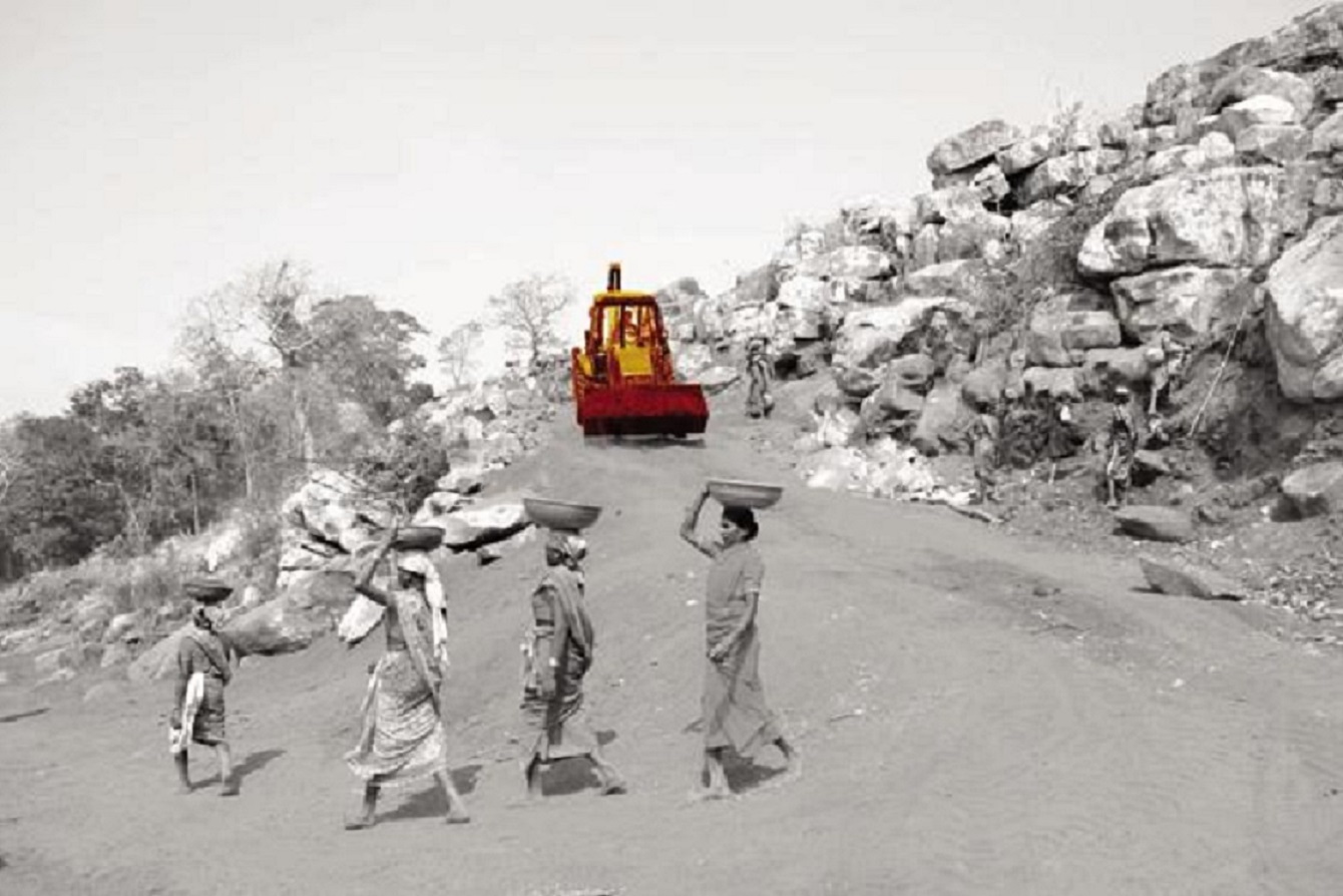 A few women carrying some baskets with a bulldozer in the background