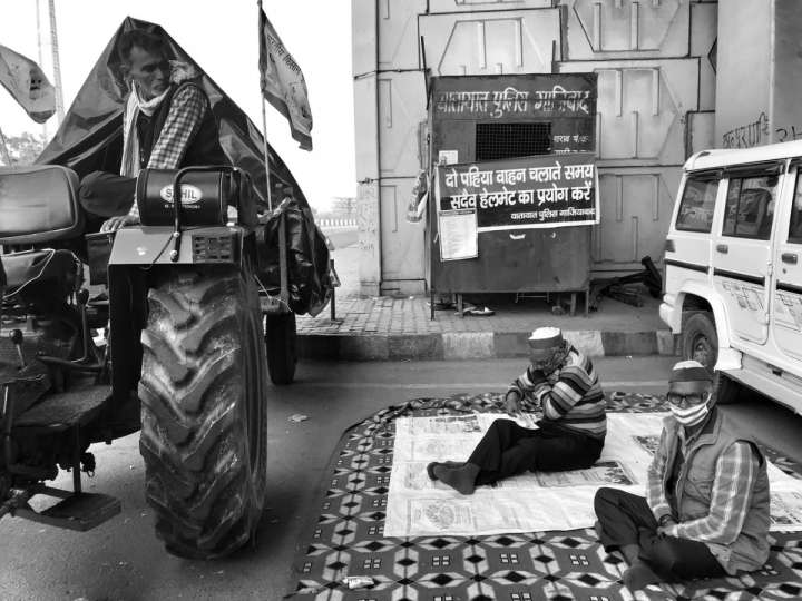 People sitting on a mat in between a tractor and a car-farmers protest