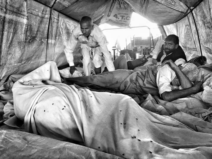 Several people lying with blankets covering them, resting and one man looking into the camera-farmers protest