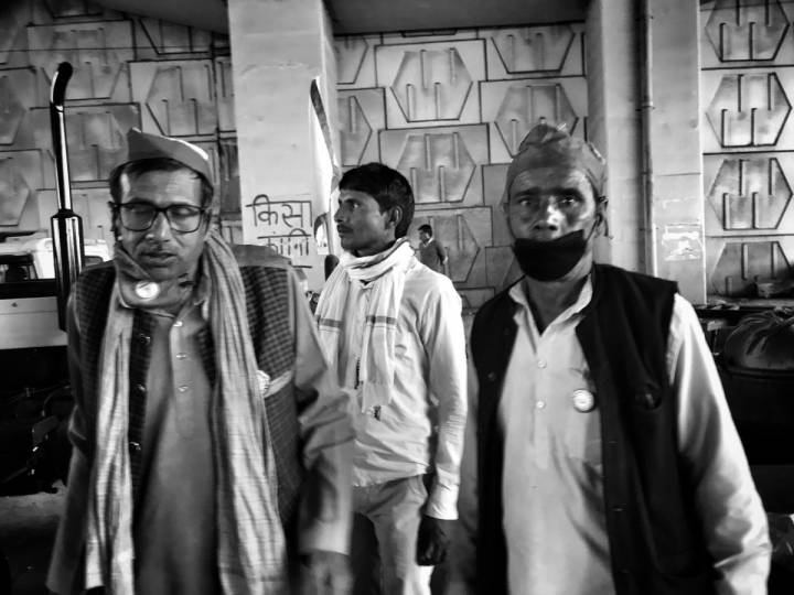 Three men wearing masks standing next to each other with vehicles in the background-farmers protest