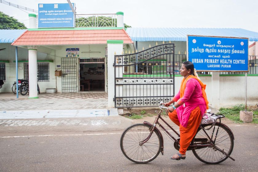woman cycling past public health centre-healthcare in India-COVID-19