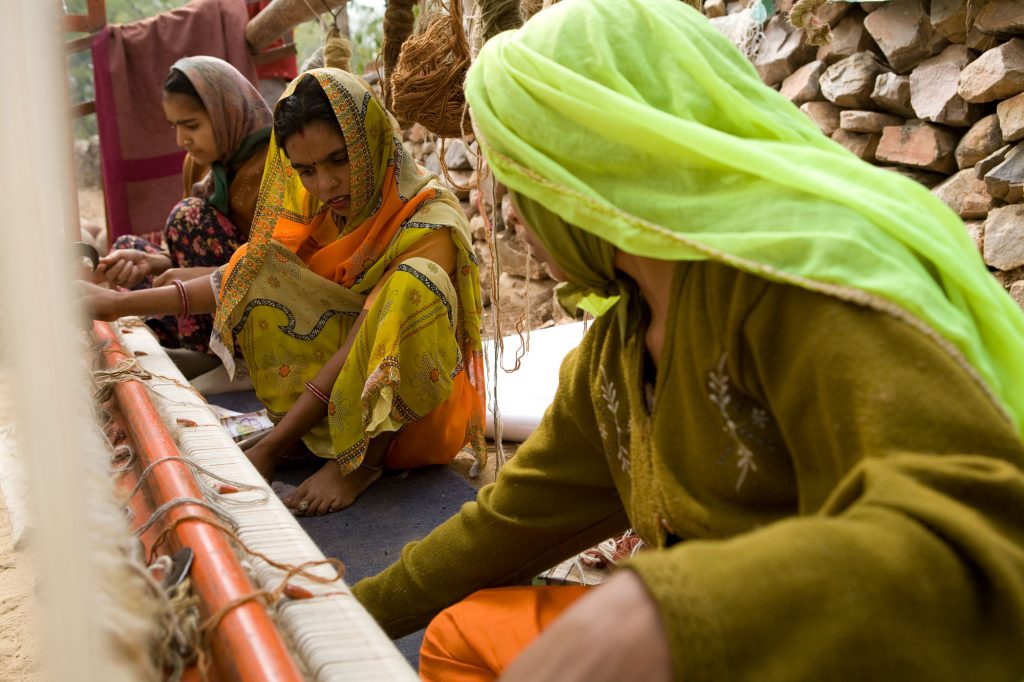 Indian women weaves carpet on a loom at Jaipur Rugs-collaboration