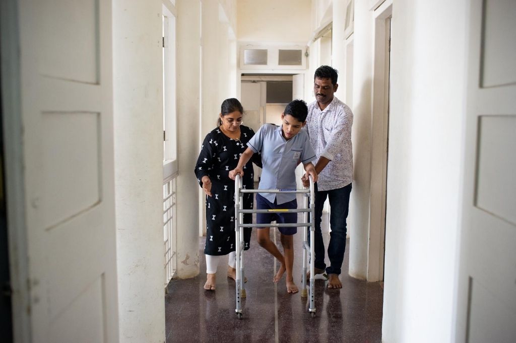 A child with disability walking with a walker with his occupational therapist and another person assisting him. Since COVID-19 struck, therapists working with children with disabilities have had to change their ways