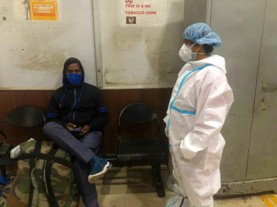Monika Mandal wearing a PPE standing next to a seated masked man-ward worker