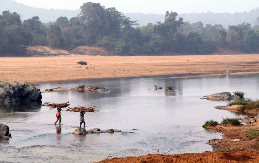 two members of the Madia Gond tribe  in Gadchiroli carrying fuelwood and crossing a river