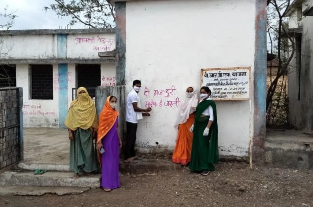 group of people standing in front of a wall which has a slogan about social distancing painted on it-NGOs