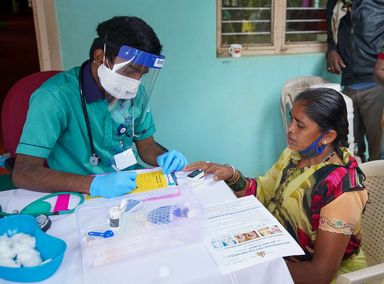 A woman getting her oxygen levels checked by a man wearing a mask and face shield_courtesy_Trinity Care foundation_Flicr_COVID-19_second wave_vaccine hesitancy