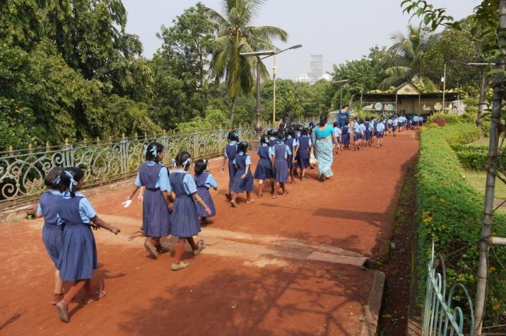 Girls wearing a uniform walking in a line in a garden-adolescent girls COVID-19 education