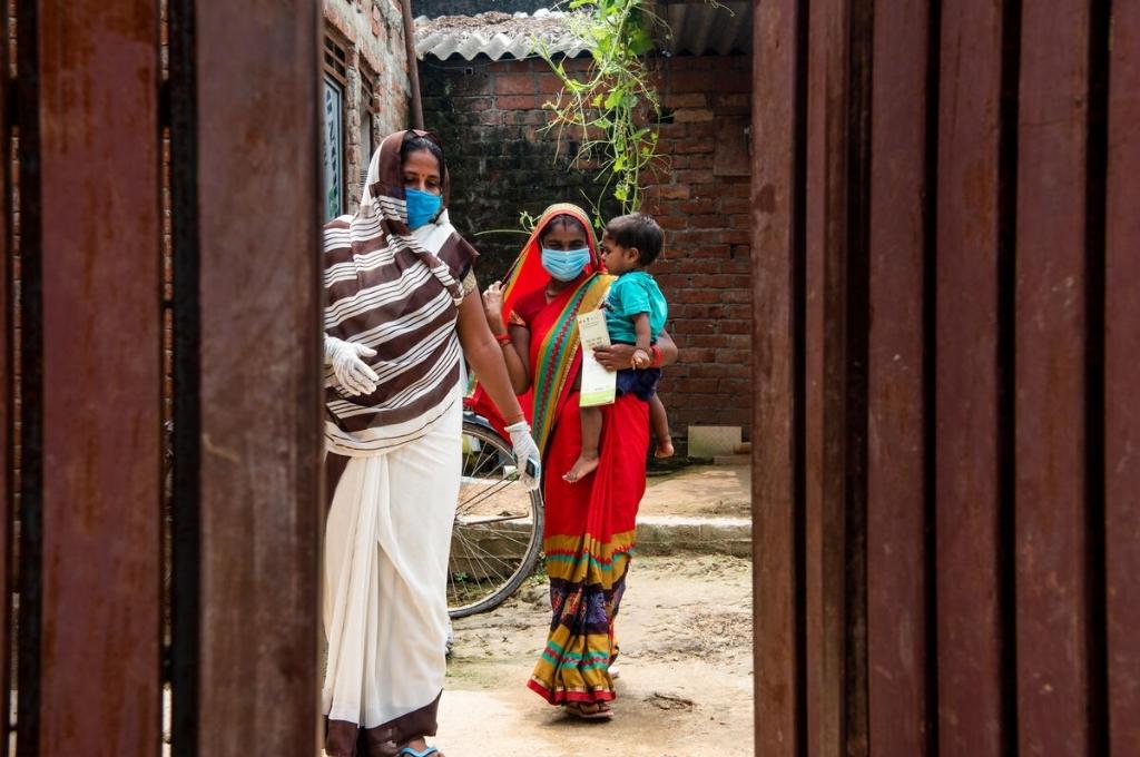 two masked women standing; the woman to the right has a baby in her arms-