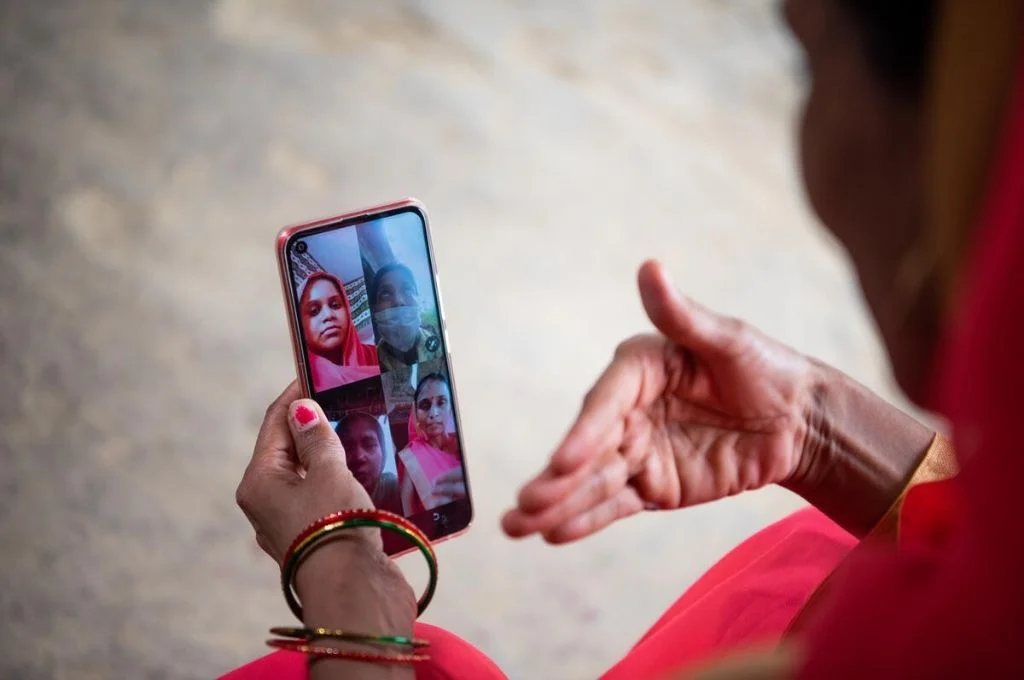 an aanganwadi worker video calling a group of women beneficiaries on a smartphone for telecounselling-COVID-19 awareness campaigns