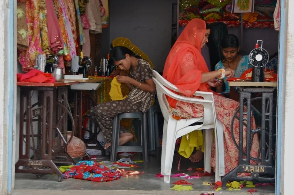four women sitting on chairs on a fabric shop working on stitching clothes in a tailor shop-livelihoods programmes