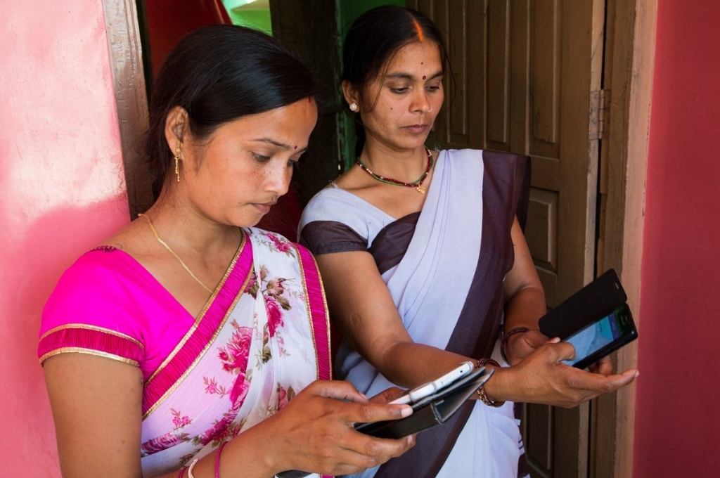two women, one on the right looking at her smartphone and the one on the left looking at a tablet, using an App-unorganised sector