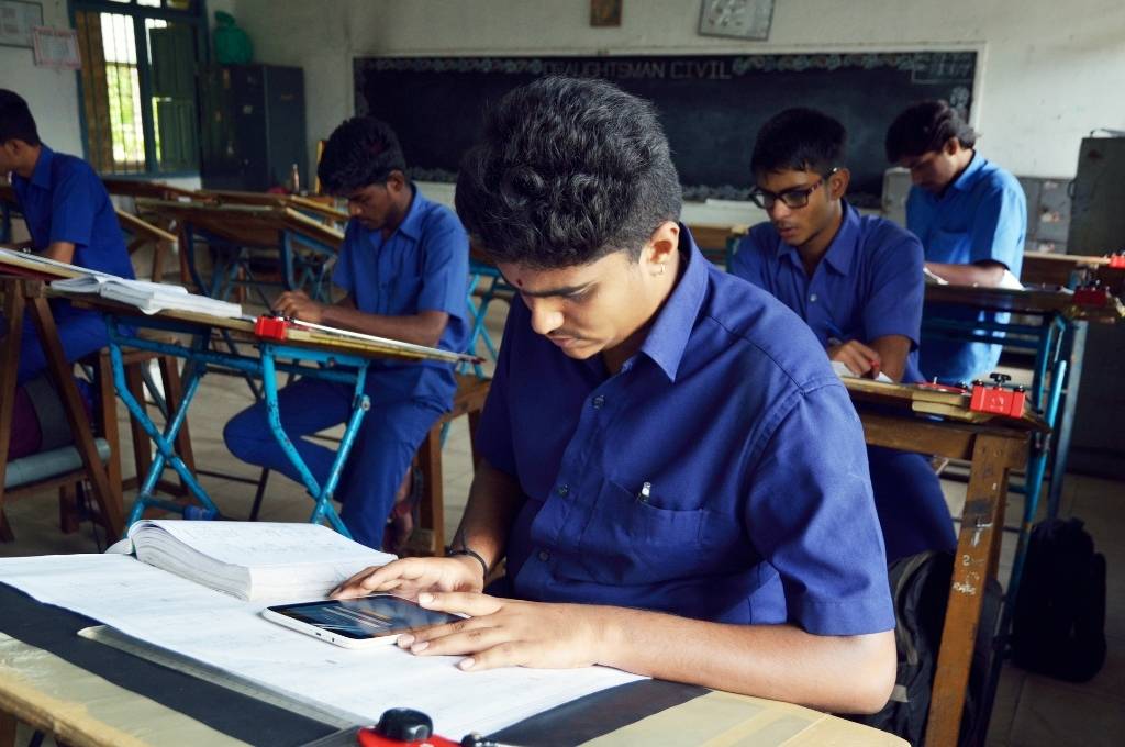 A boy sitting on a desk with a tablet, performing technical task-India's youth-job