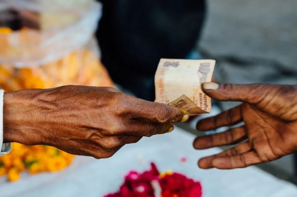 A ten rupee note being exchanged from one hand to another against a blurred background with flowers. Here's what you need to know about tax exemptions, FCRA rules, and more, if you plan to raise money through a crowdfunding platform.
