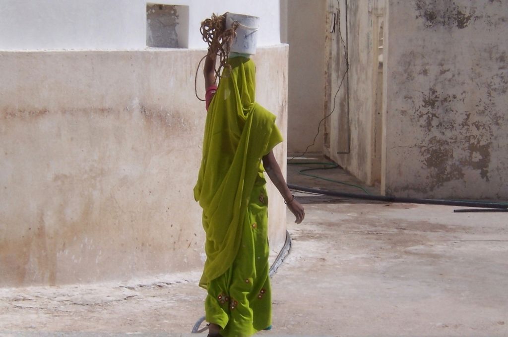 A woman in a green saree carrying construction material on her head. Multidimensional poverty index takes into account poverty beyond a lack of income
