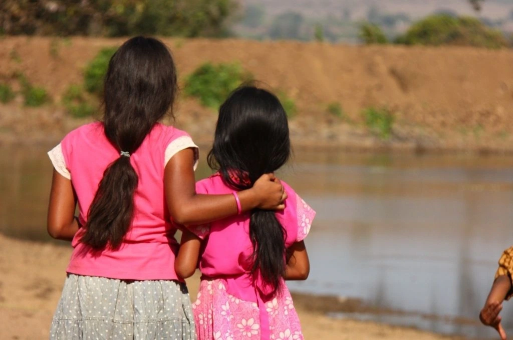 Two young girls with their backs turned towards the camera looking at a water body_adolescent women