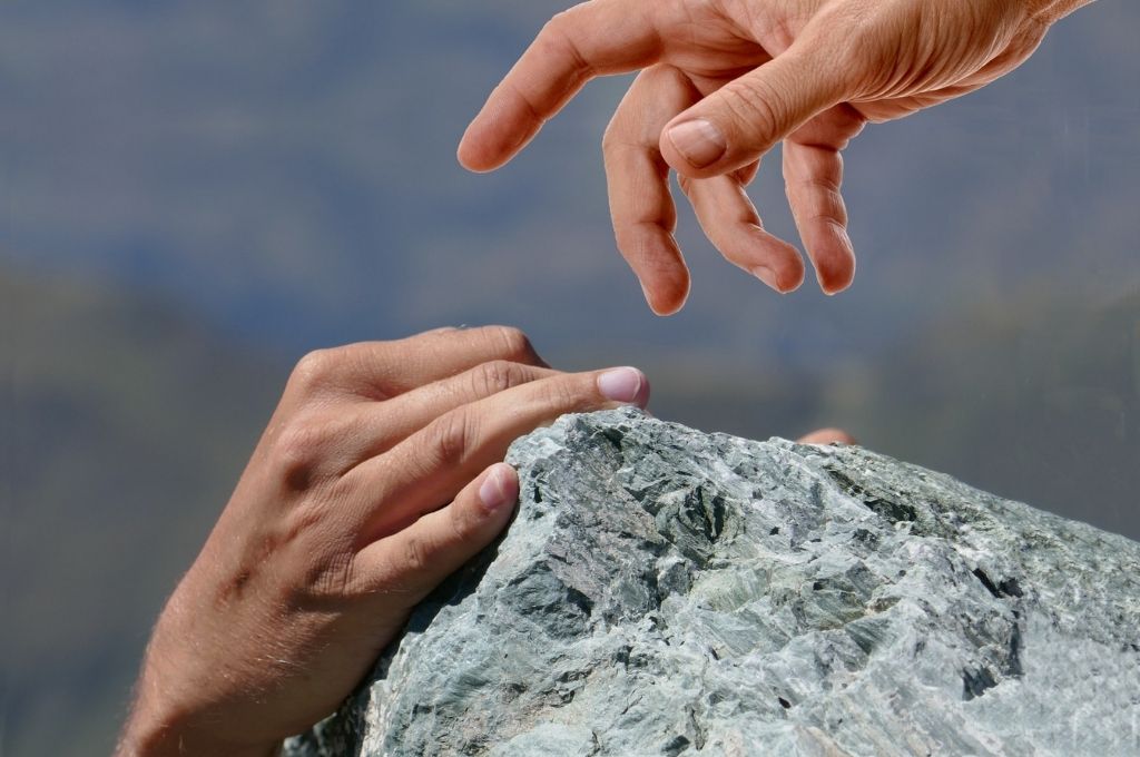 A hand reaching out to hold another on a rock. Budget 2022 can encourage citizens to donate to nonprofits