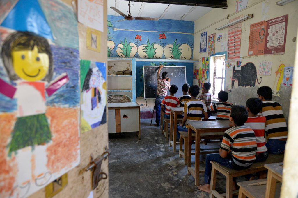 Young children sitting in a classroom, where one boy is writing on the blackboard - Budget 2022