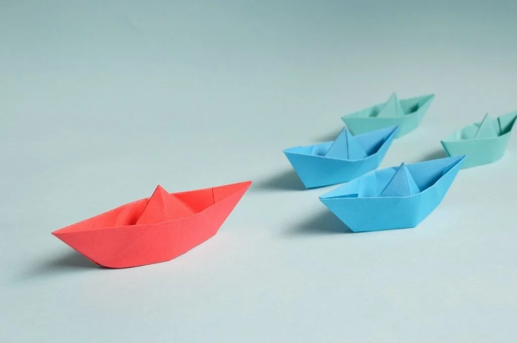 One red paper boats followed by two blue boats and two green boats. A recent report unpacks the challenges around people management in the social sector, and what can be done about them | Pexels
