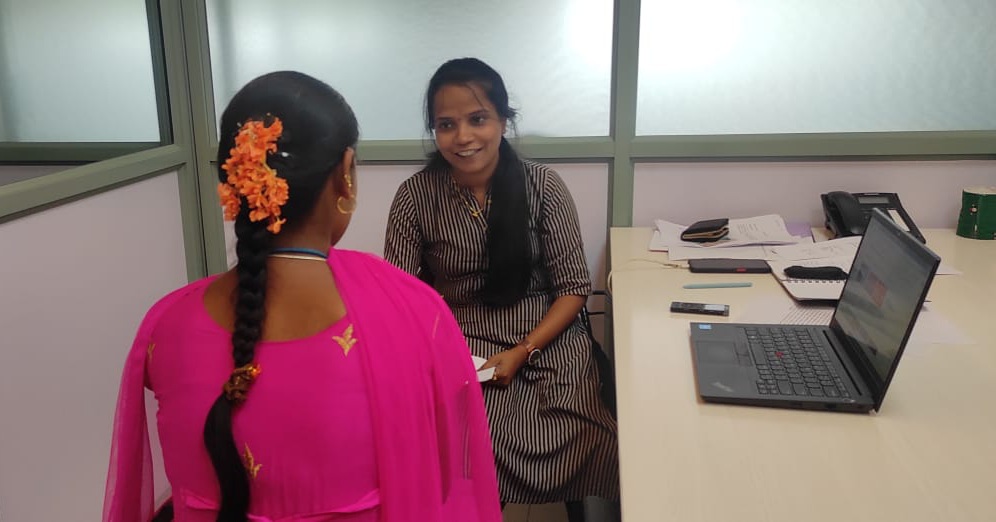 Shaila, an enumerator with Good Business Lab is seated at a table where she is conducting an survey with an employee at a garment factory