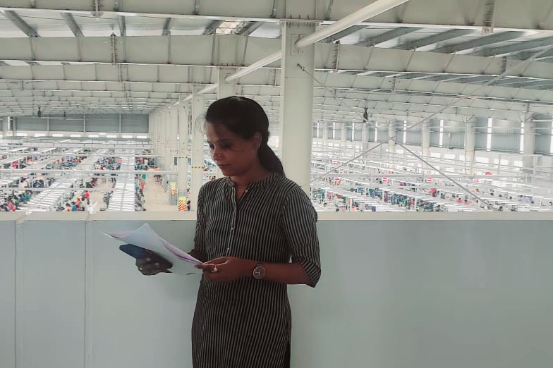 Shaila, an enumerator at Good Business Lab is standing in a garment factory and reading a report