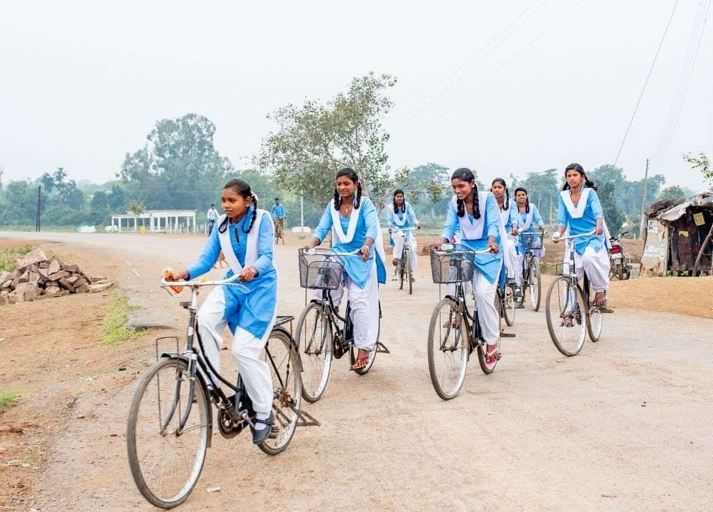Three girls in blue and white school uniforms on bicycles. Why does child marriage persist in Bihar