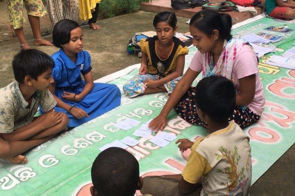 A teacher sitting on the floor surrounded by students-unpaid work