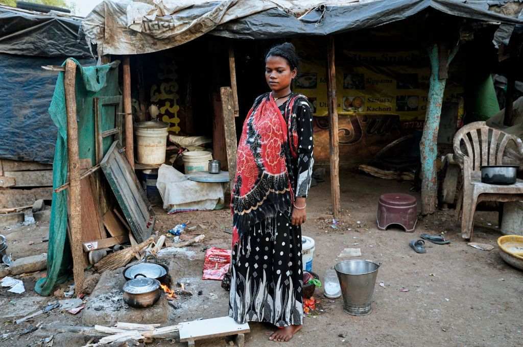 A woman stands surrounded by utensils and a firewood chulha_air pollution
