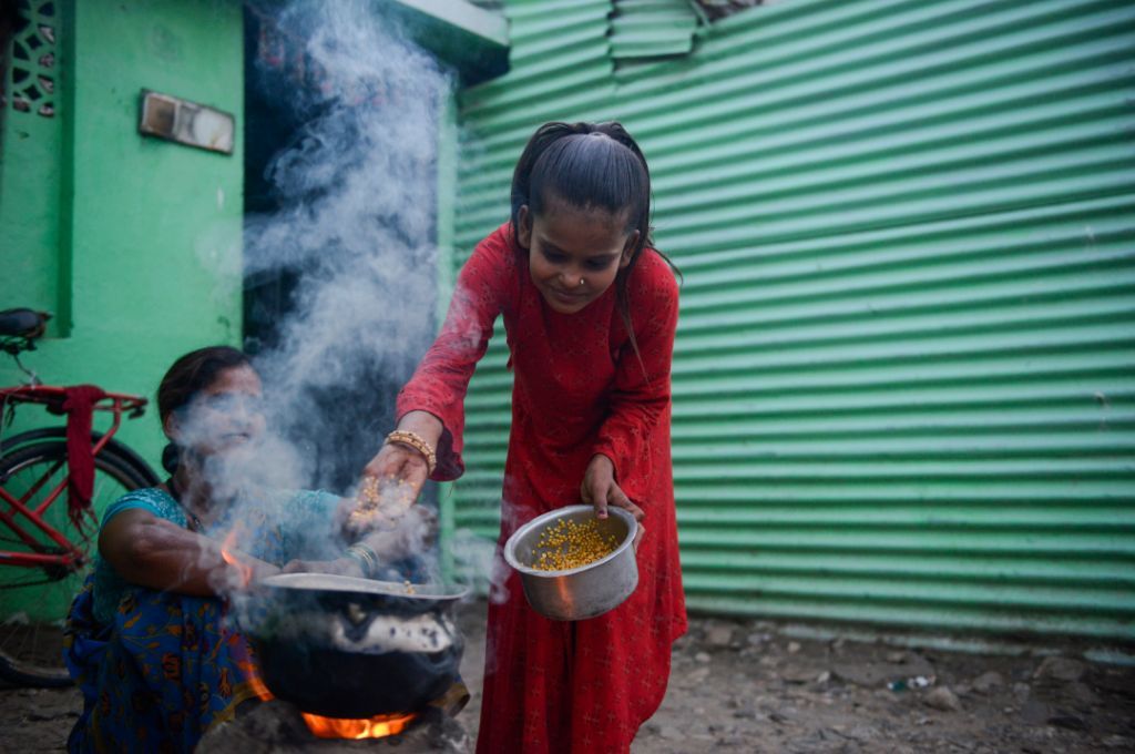A young girl puts ingredients into a pot placed on a firewood chulha while a woman watches_air pollution