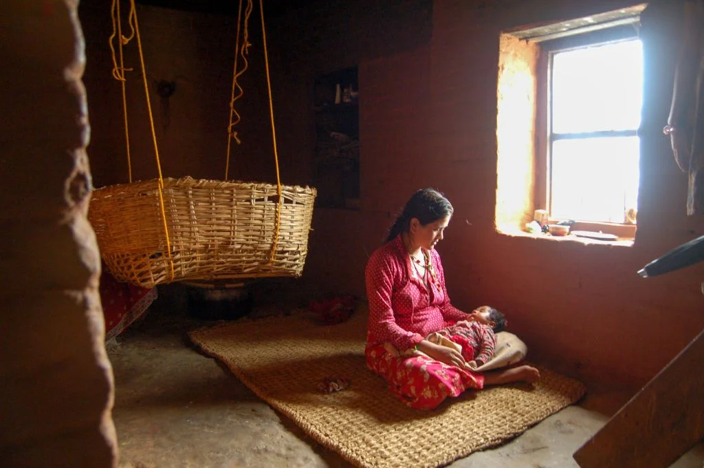 A mother with an infant on her lap and a bamboo crib hanging behind them_losing young mothers to suicide