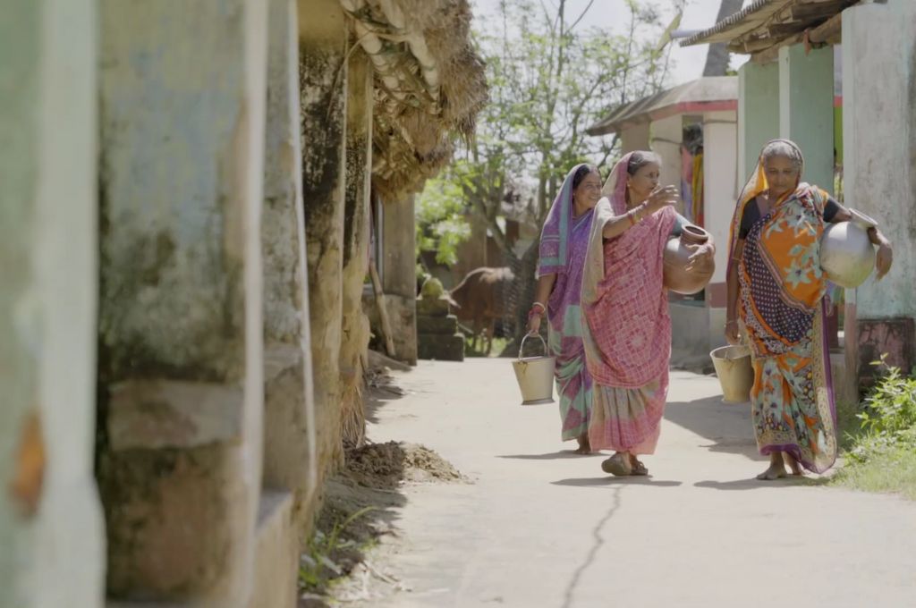 Three women in sarees walking with water vessels-reforestation