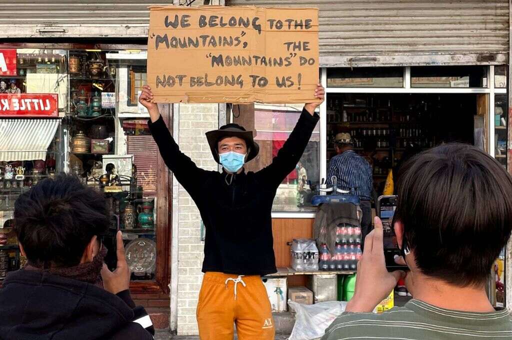 A man holding a placard in a market while two other men click his photos on their mobiles_environmentalist in Leh