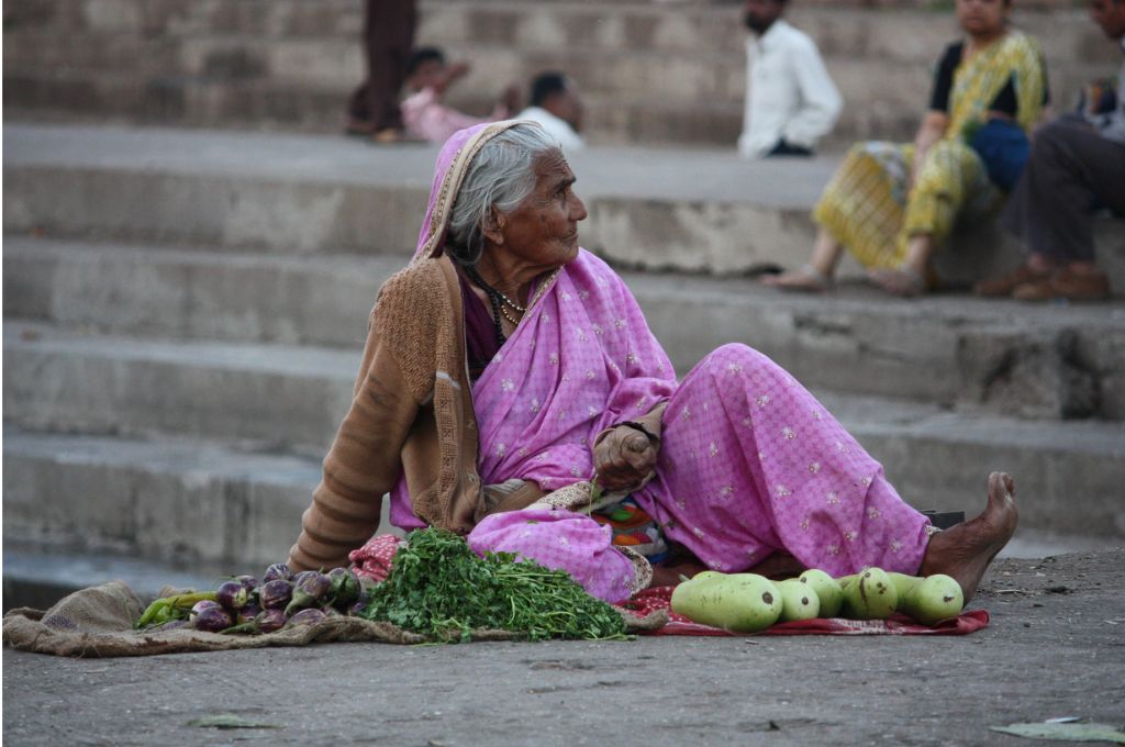 An old woman wearing a saree sitting on some steps with some vegetables_discrimination