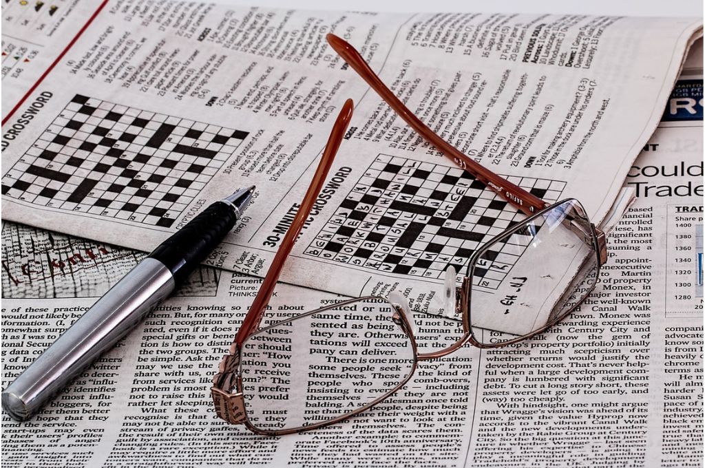 Picture of a pair of spectacles and a pen on top of a newspaper with a half-filled crossword