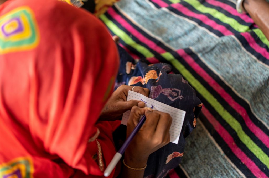 A woman with her head covered in a saree writing on a piece of paper_Jan Aadhaar