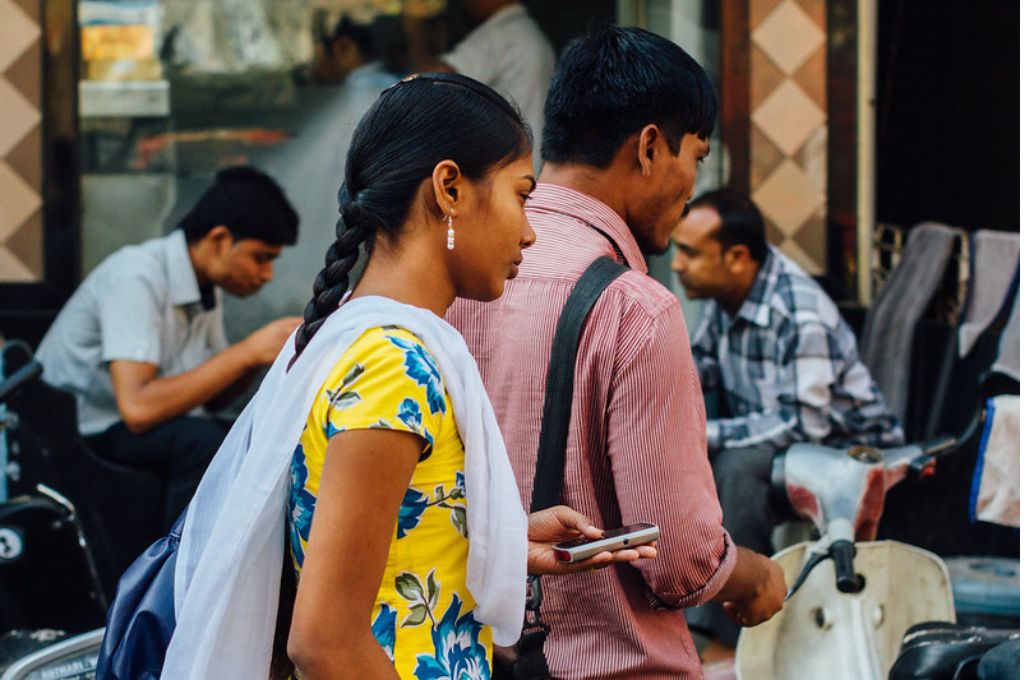 Indian woman with a smartphone standing behind a man_women labour force participation