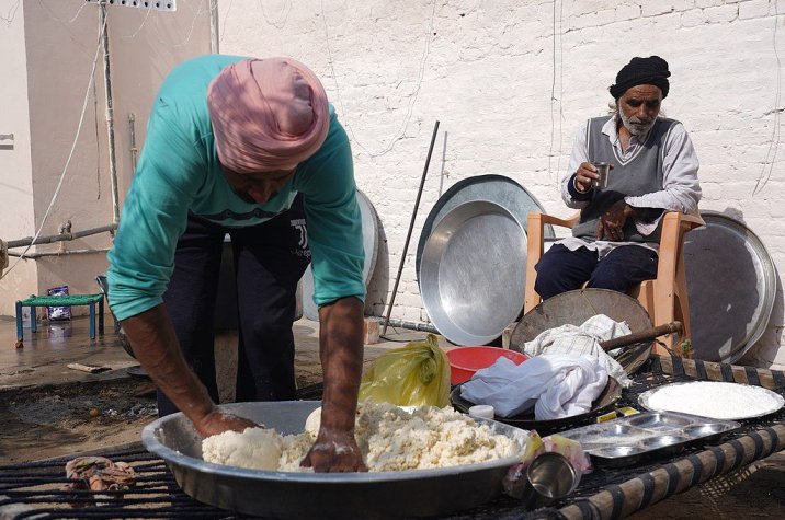 an elderly man looks on as another man kneads dough--disabled people