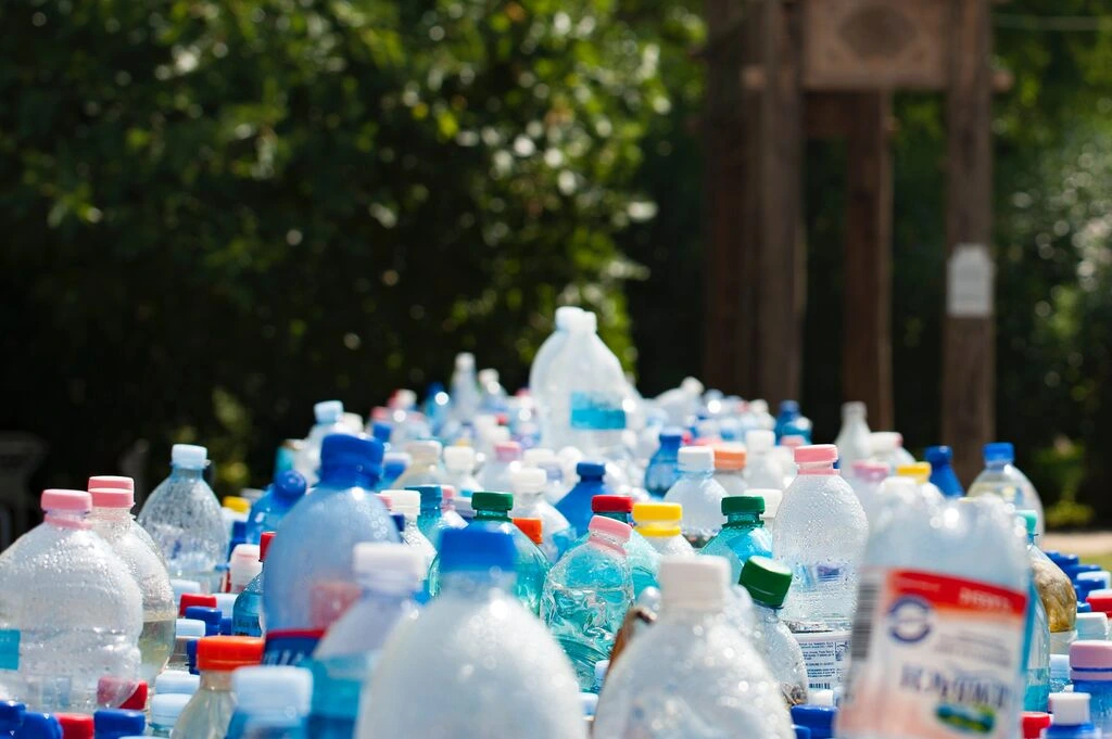 The image is a close-up shot of several rows of disposable plastic water bottles placed in an outside setting._Waste
