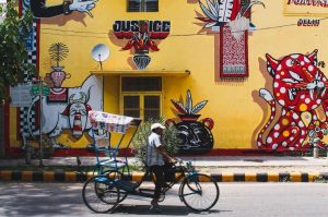 A man riding a rickshaw with a yellow graffitied wall in the background that says justice-denotified tribes