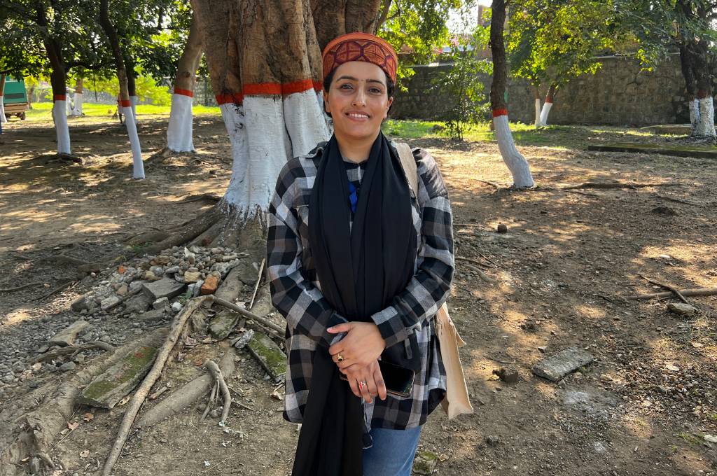 A woman wearing a cap, a shirt and blue jeans standing in front of a tree--tribal women