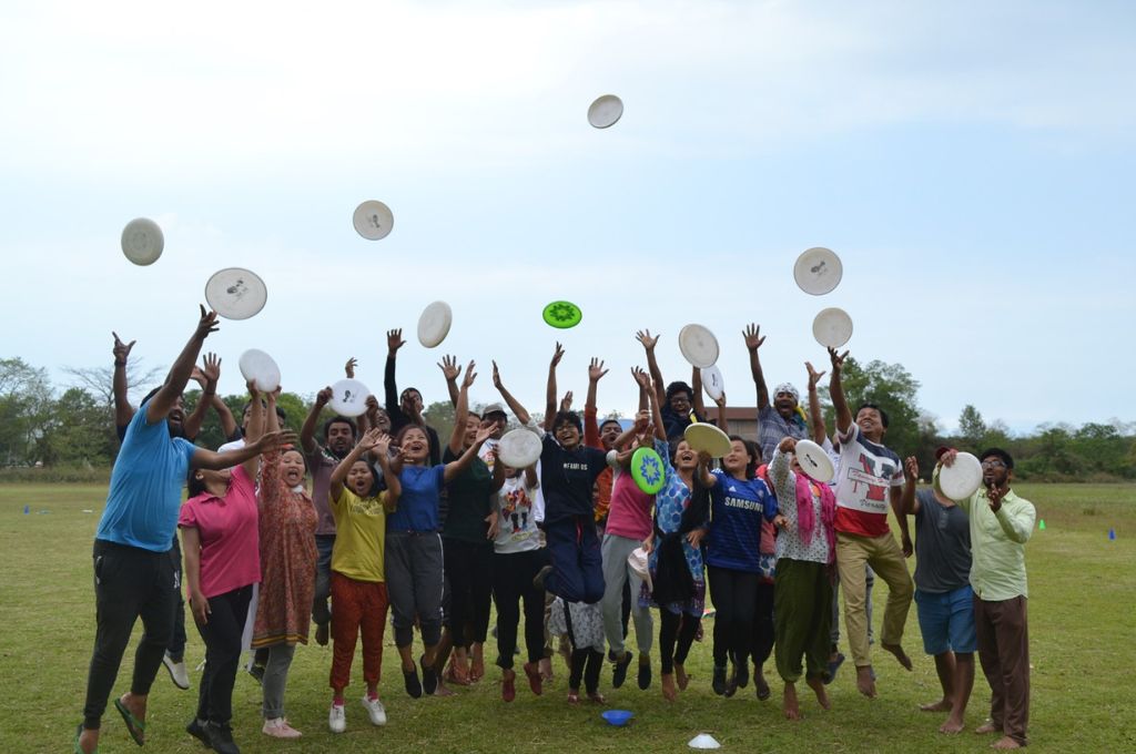 A group of people of varying ages and genders throwing frisbees up in the air--ultimate frisbee